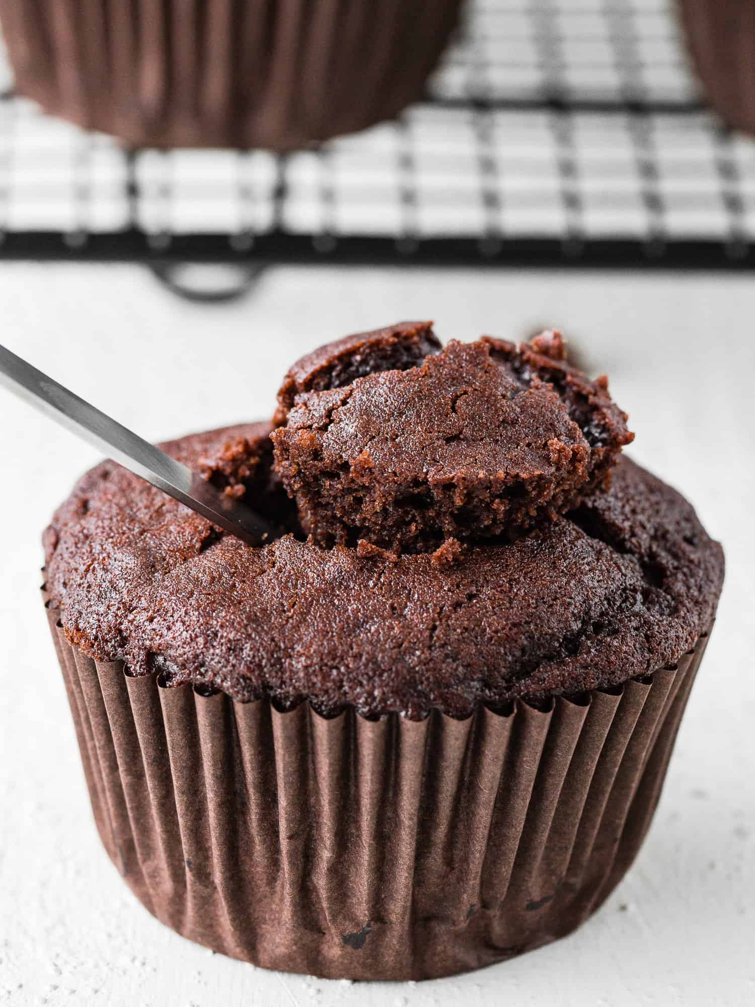 a knife pulling out the center core of an eggless chocolate cupcakes. 