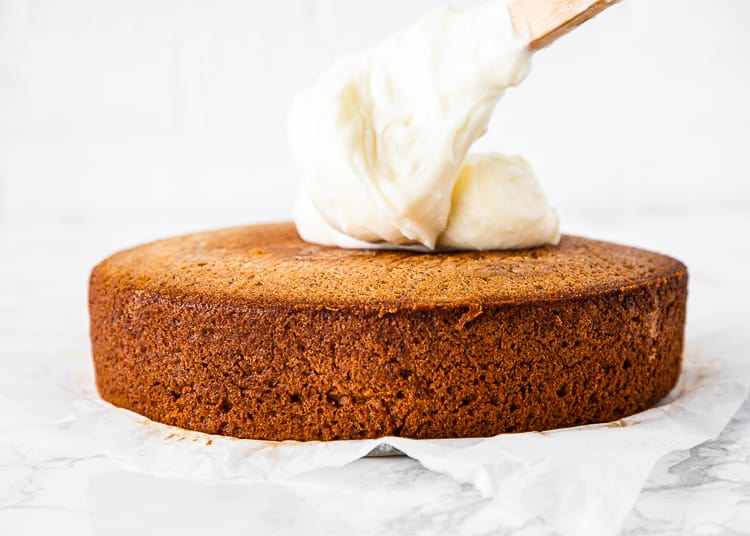 egg-free banana cake with a big dollop of cream cheese frosting on top over a marble surface. 