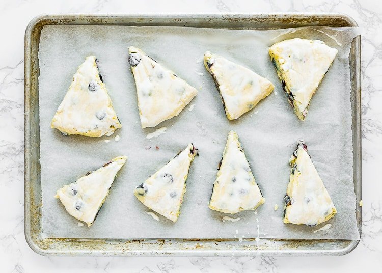 Eggless Blueberry Scones  dough wedges brushed with heavy cream over a baking tray.