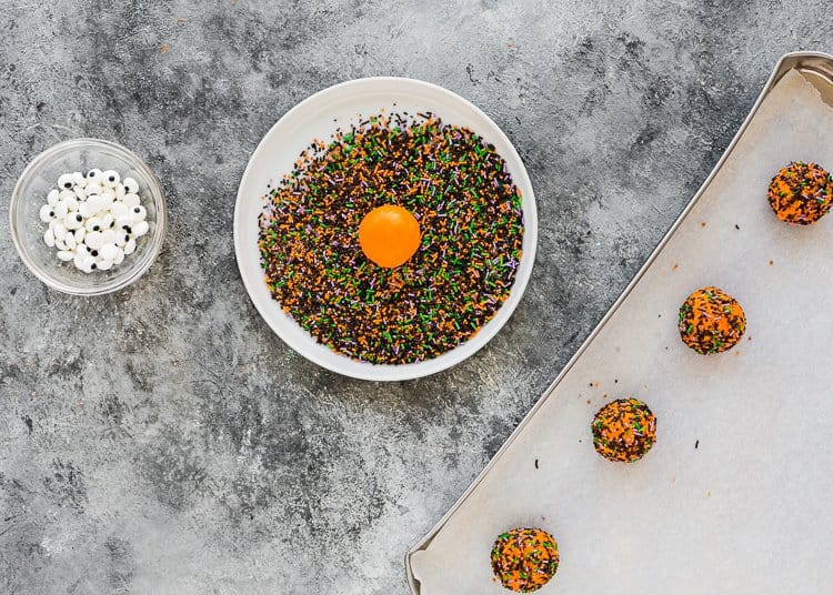 egg-free sugar halloween cookies being covered in sprinkles. 