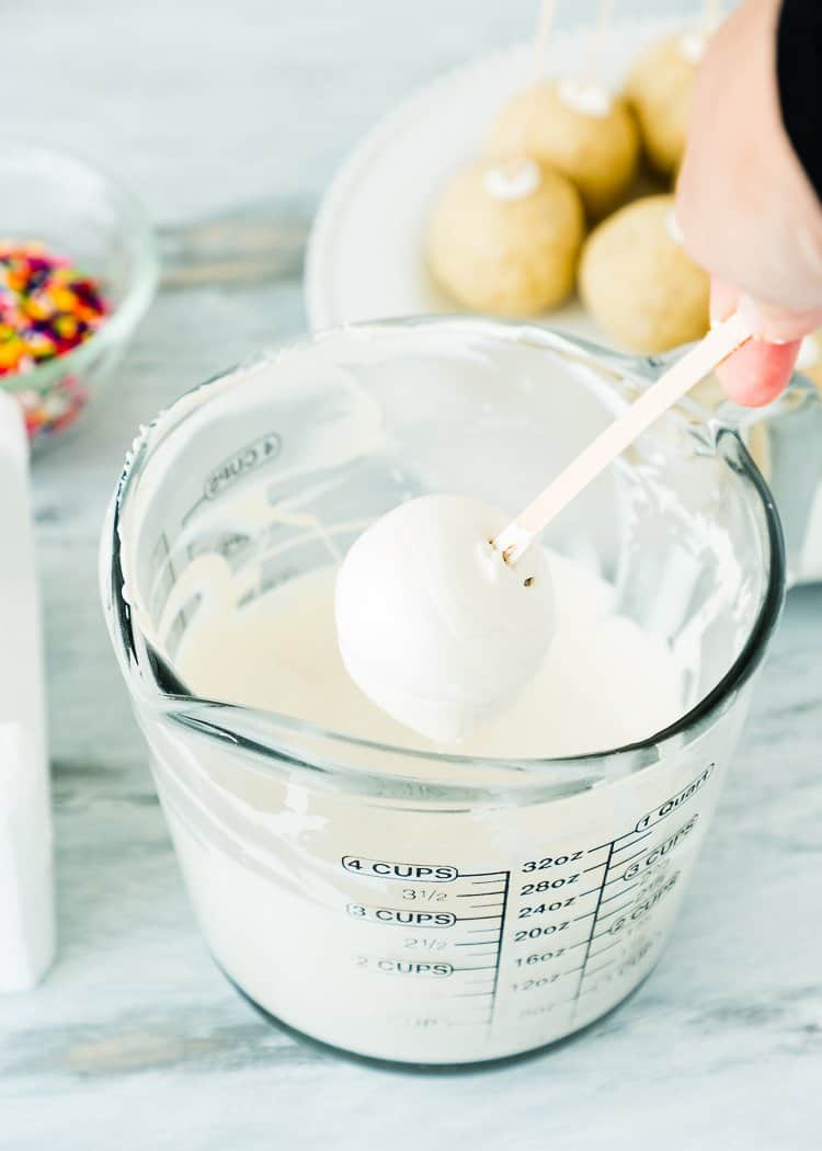 an eggless cake pop being covered with melted candy melts.