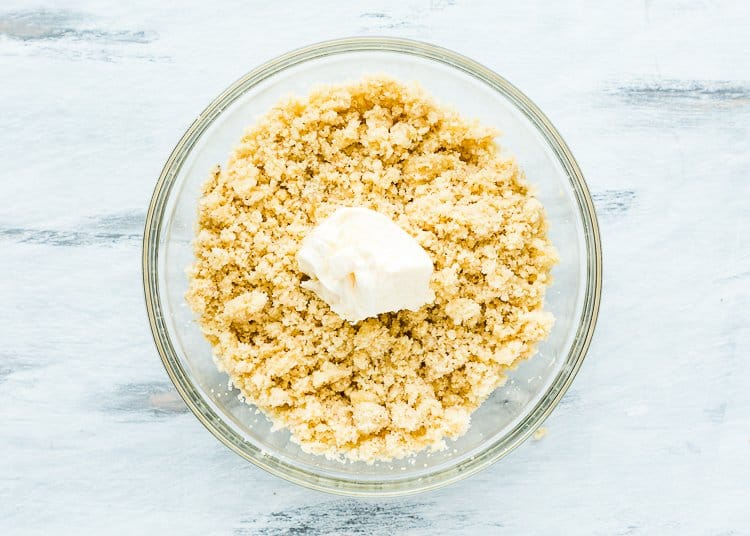 Crumbled Eggless Homemade Cake in a bowl with frosting on top. 