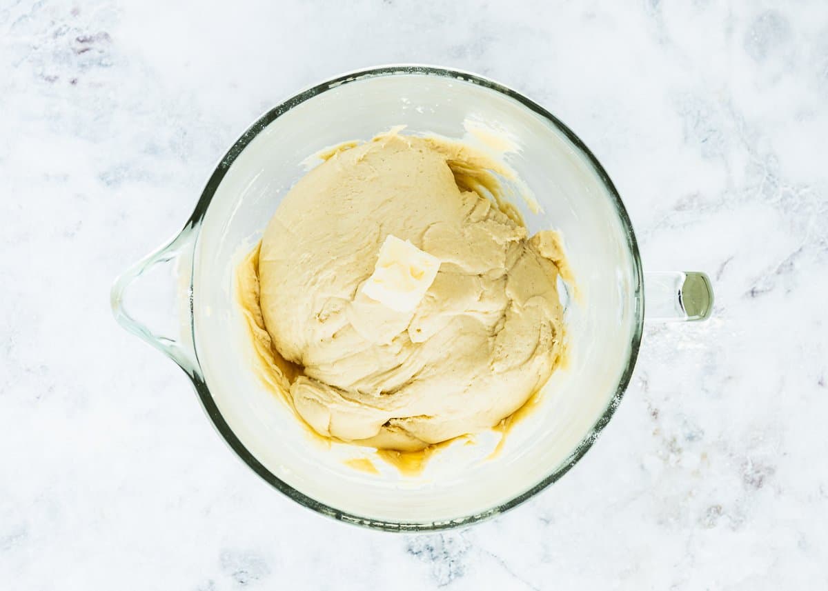 smooth egg- brioche dough in a bowl with butter on top. 