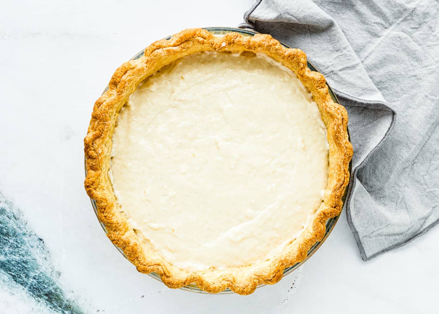 Eggless Coconut Cream Pie in a pie dish with a grey kitchen towel on the side. 