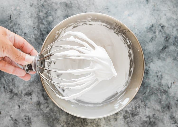 a hand holding a whisk with Homemade Eggless Marshmallow Fluff. 