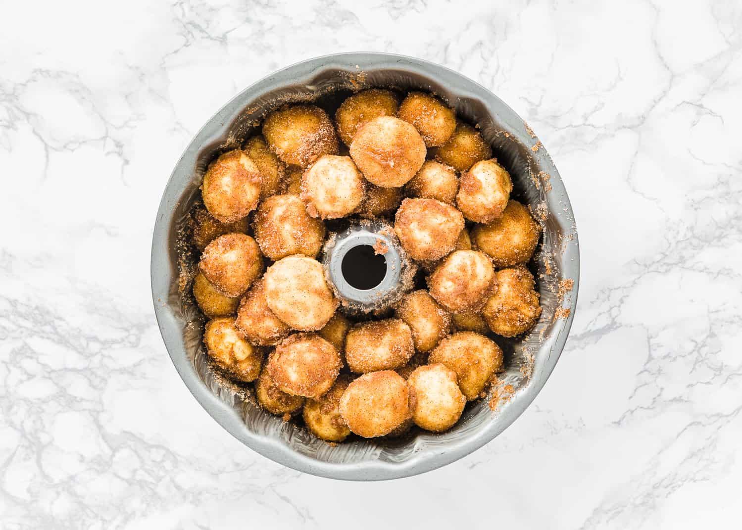 Egg-free monkey bread dough balls coated with melted butter and cinnamon sugar in a bundt cake pan. 