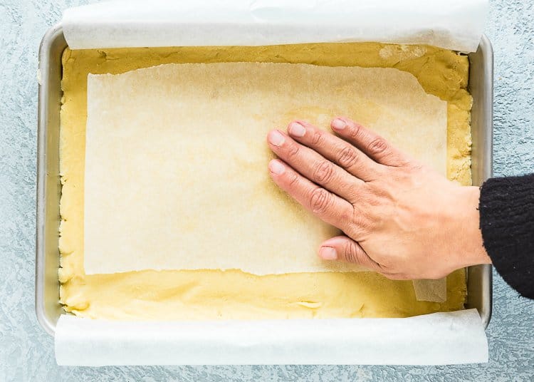 a hand spreading the dough to make lemon bar crust in a baking pan.