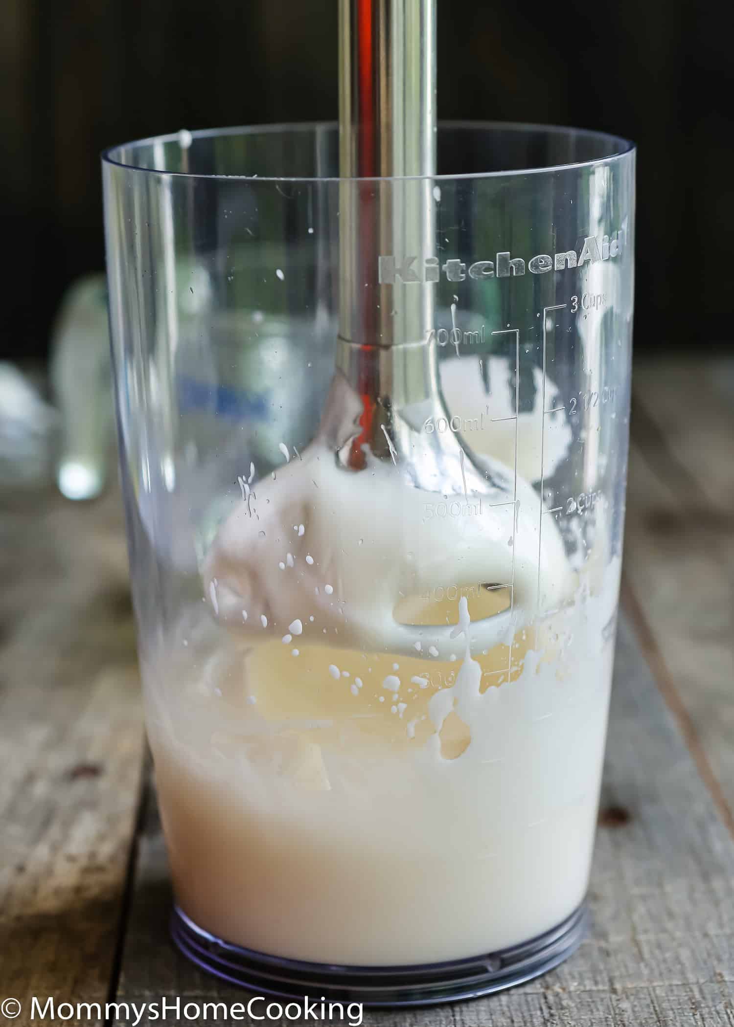 an immersion blender into a cup with eggless mayonnaise.