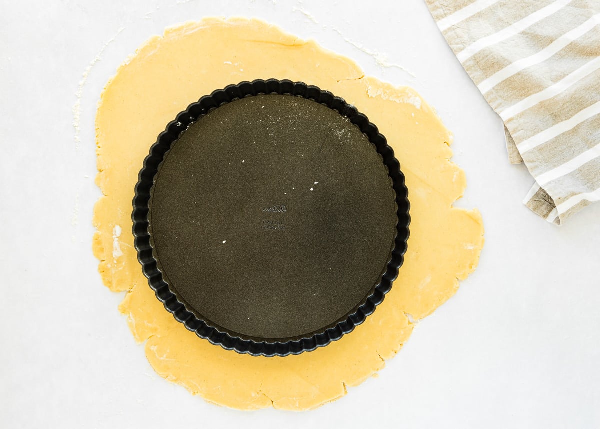 eggless tart dough on a floured surface with with a tart pan on top. 