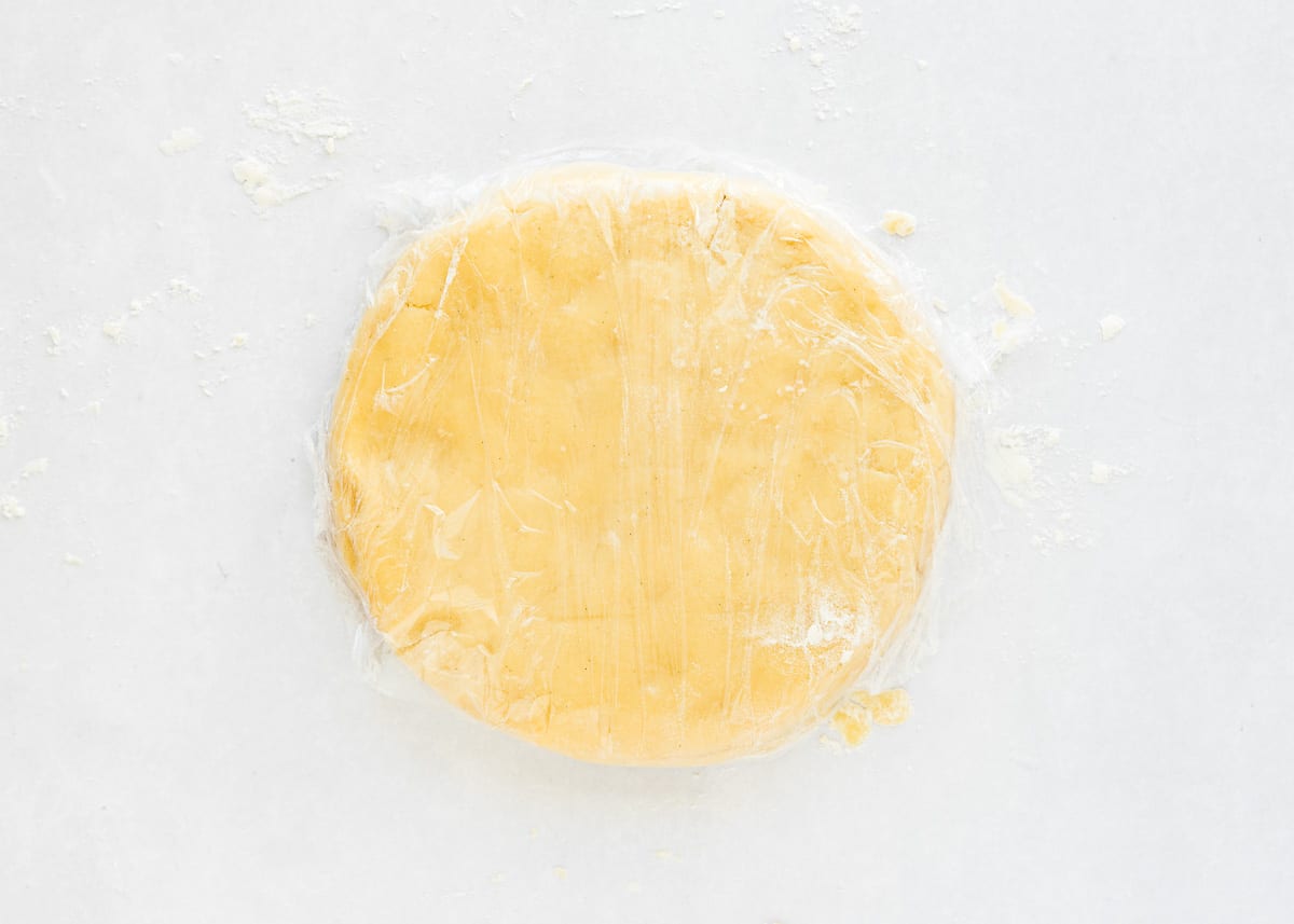 eggless tart dough formed into a disk and wrapped with plastic wrap. 