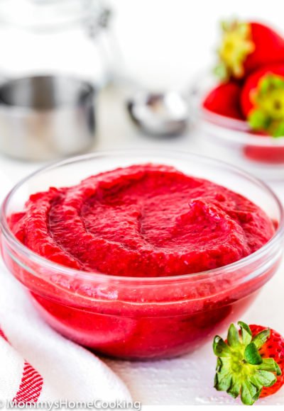 homemade strawberry puree in a glass bowl with a fresh strawberry in the side.