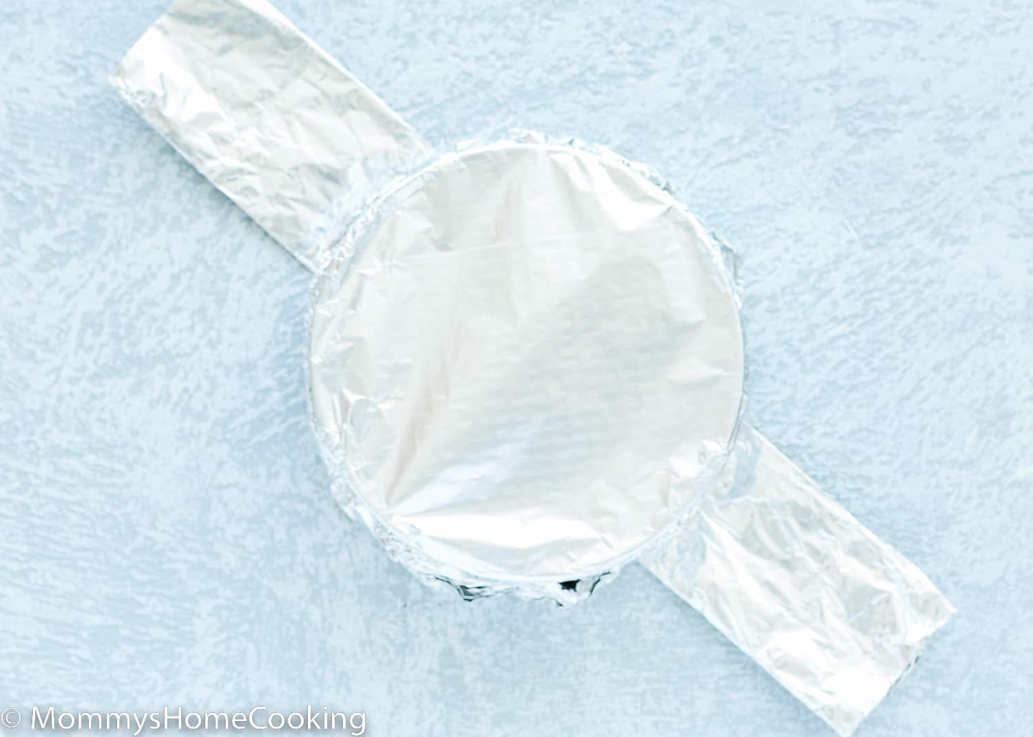 a springform pan wrapped in foil over a foil sling.