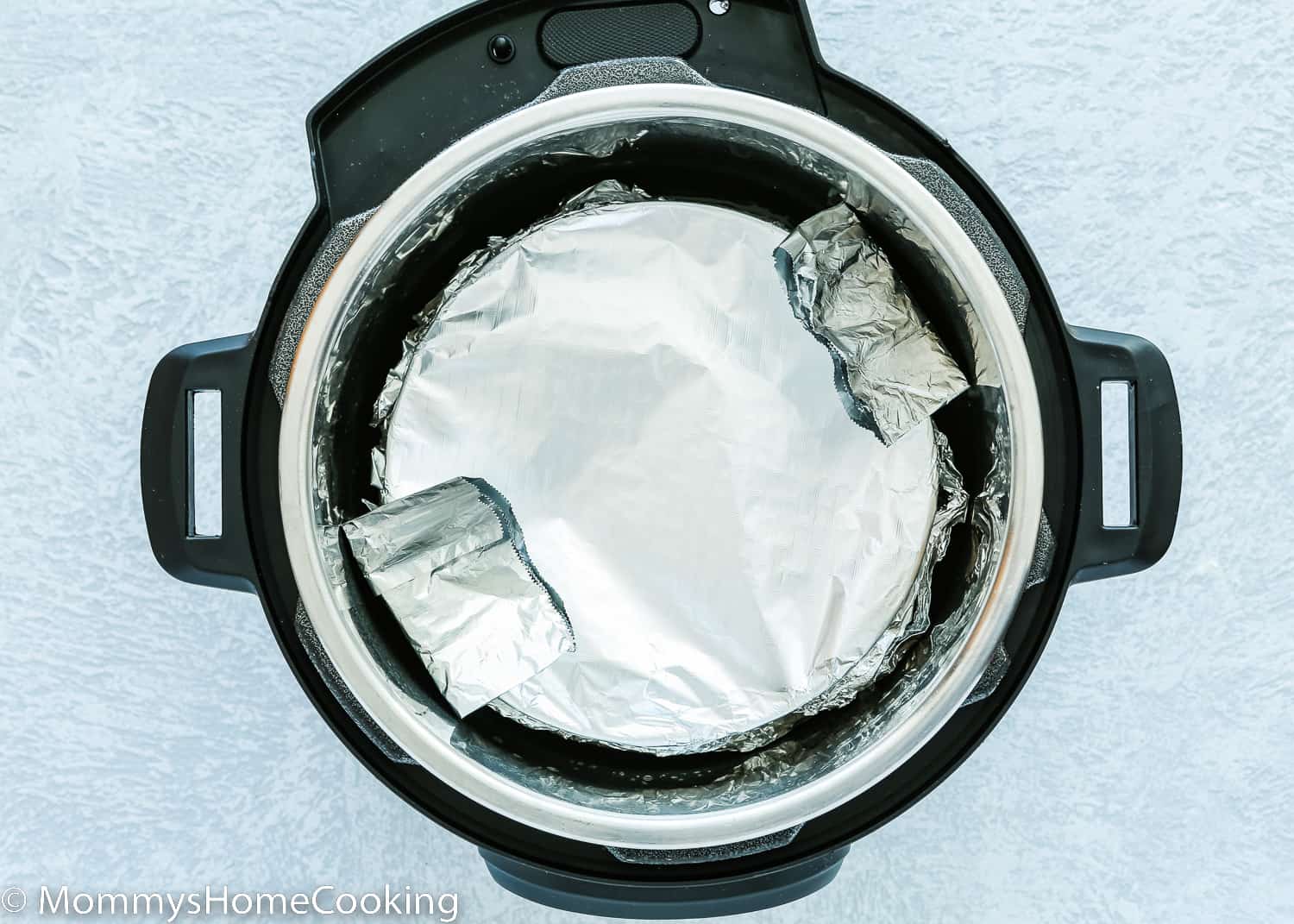 an instant pot with a springform pan wrapped in foil inside.