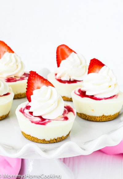 Mini Yogurt Strawberry Cheesecake with whipped cream and a fresh strawberry on a cake stand.