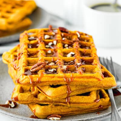 egg-free pumpkin waffles with caramel sauce and chopped pecan on a plate with two forks on the side.