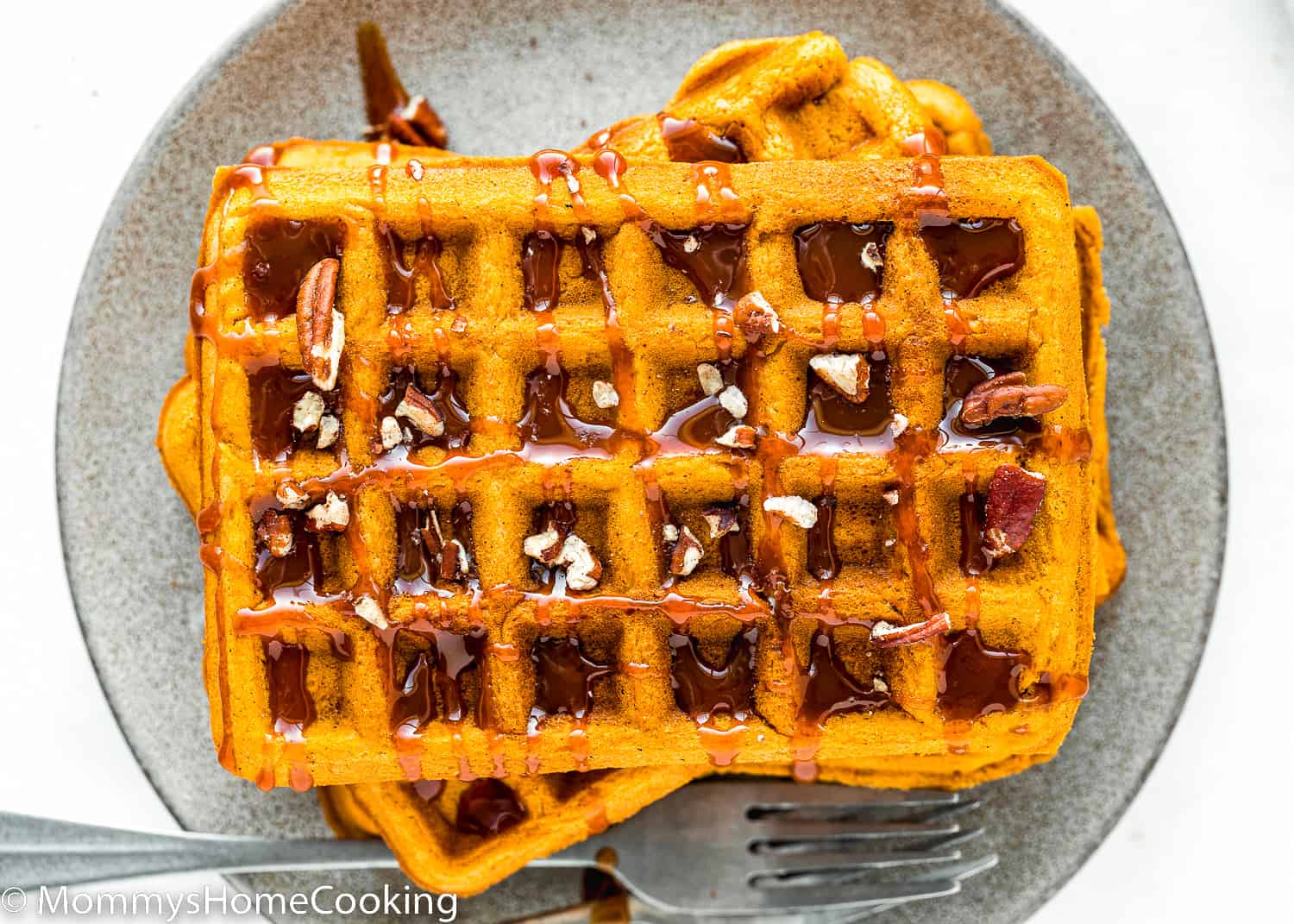 eggless pumpkin waffles with caramel sauce and chopped pecan on a plate with two forks on the side.