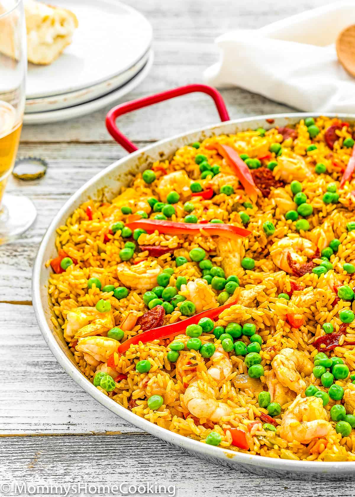 Spanish Paella in a paella pan with plate and a cup of beer in the background.