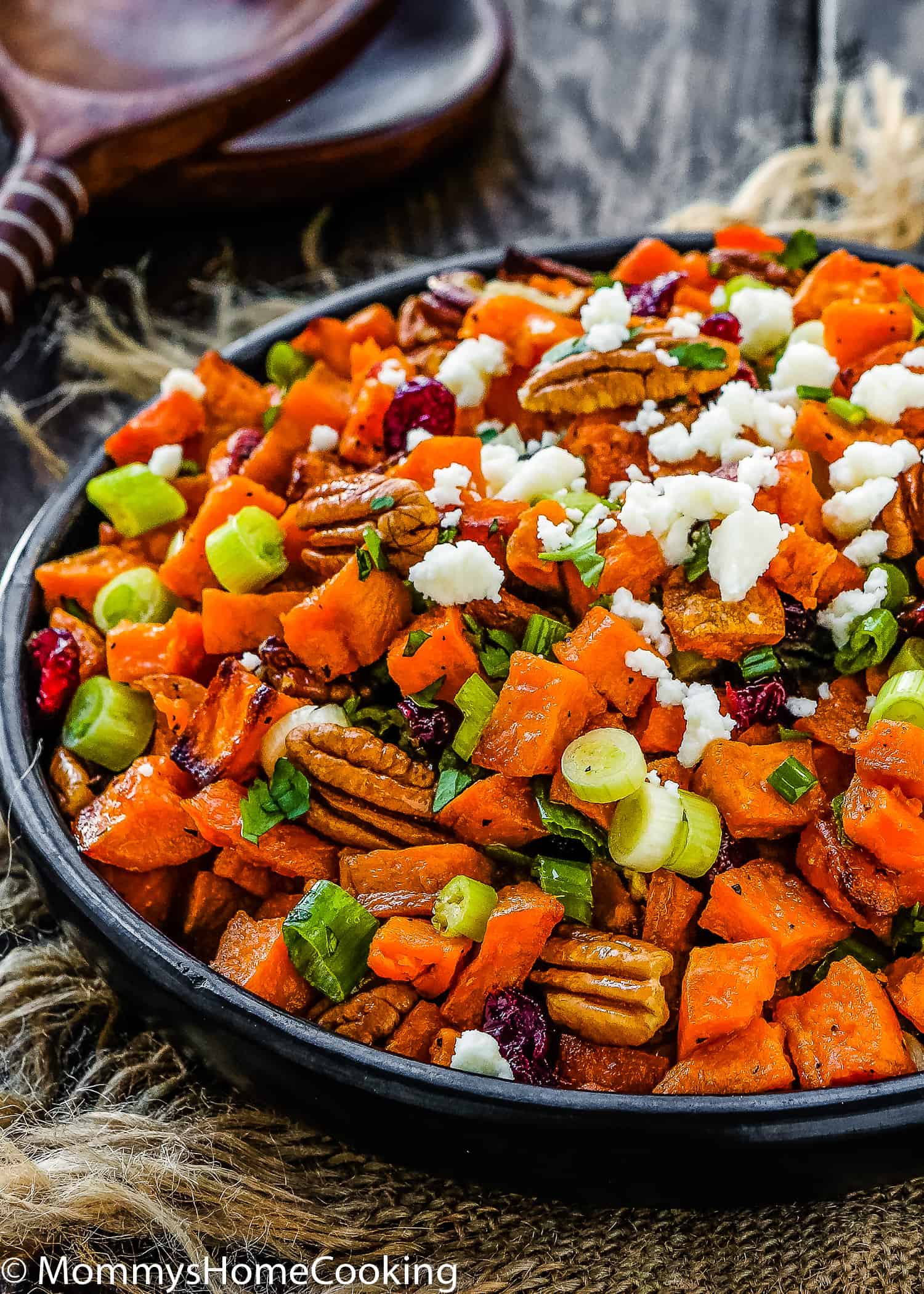 Roasted Sweet Potato and Cranberry Salad in a black serving bowl over a wooden surface and two serving spoons on the background.