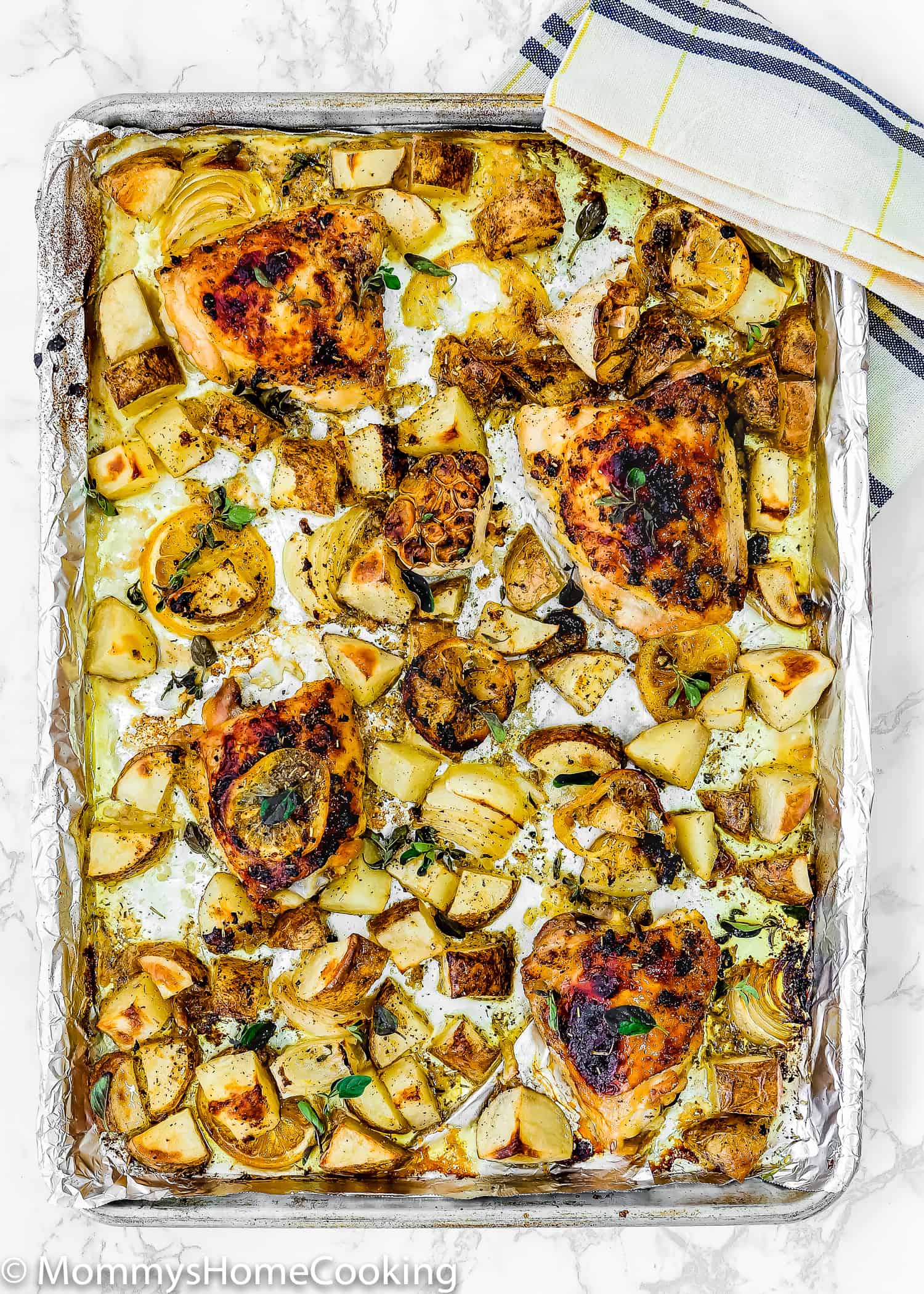  Lemon Garlic Roasted Chicken and Potatoes in a baking sheet with a kitchen towel on the side. 