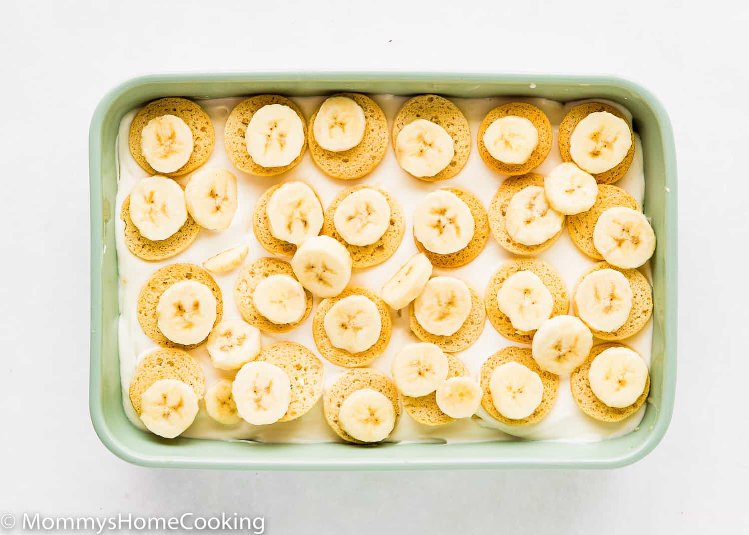 A layer of banana pudding in a rectangular green dish with homemade egg-free vanilla wafers and sliced bananas on top.