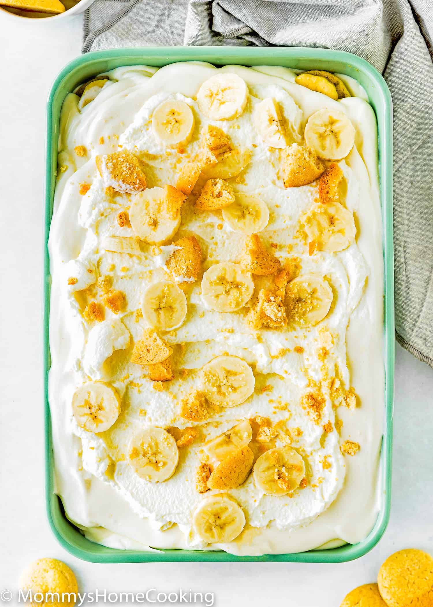 Eggless banana pudding in a green rectangular dish with a gray kitchen towel on the side.