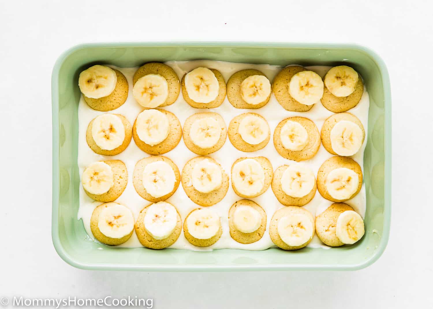 A rectangular green dish with pudding on the bottom, egg-free vanilla wafers, and sliced bananas.