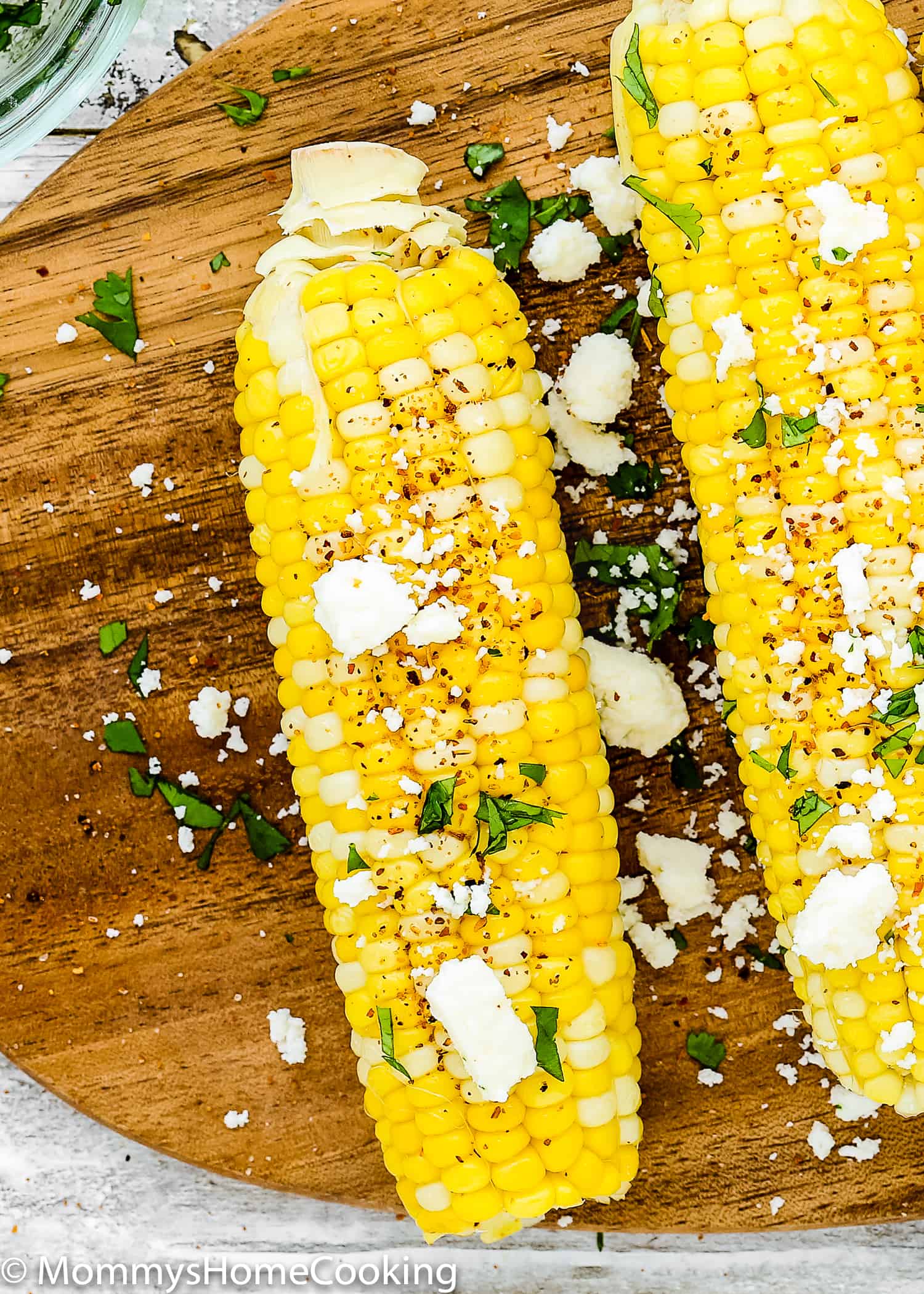 overhead view of fresh corn on the cob over a wooden tray with crumbled queso fresco, butter and tanjin and cilantro. 
