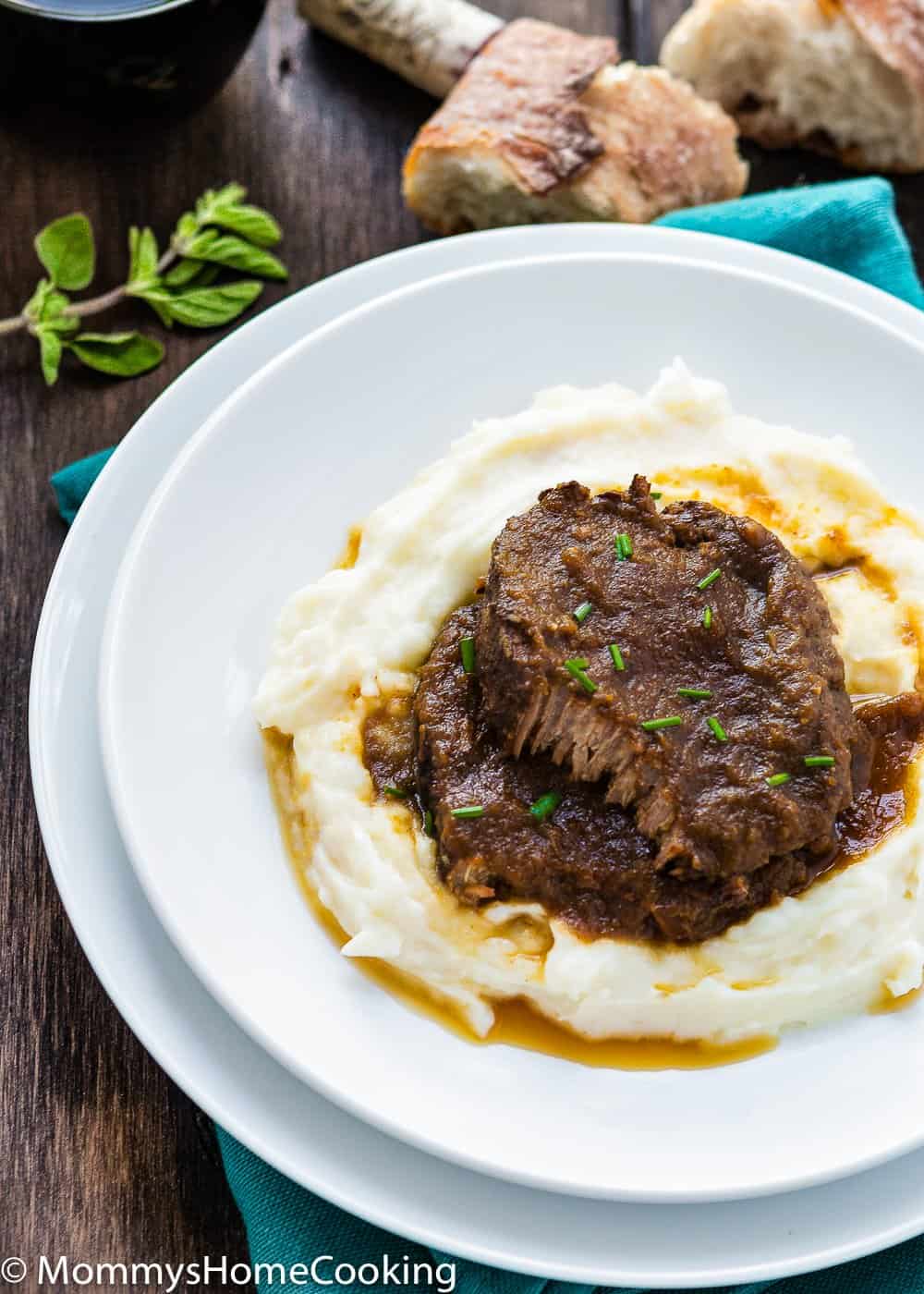 Venezuelan Asado Negro in a white plate with mashed potatoes  and garnished with chives