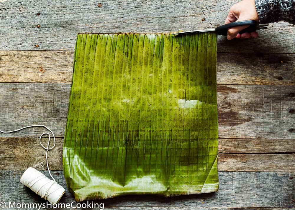 a hand cutting the center stem of the banana leaves to make hallacas.