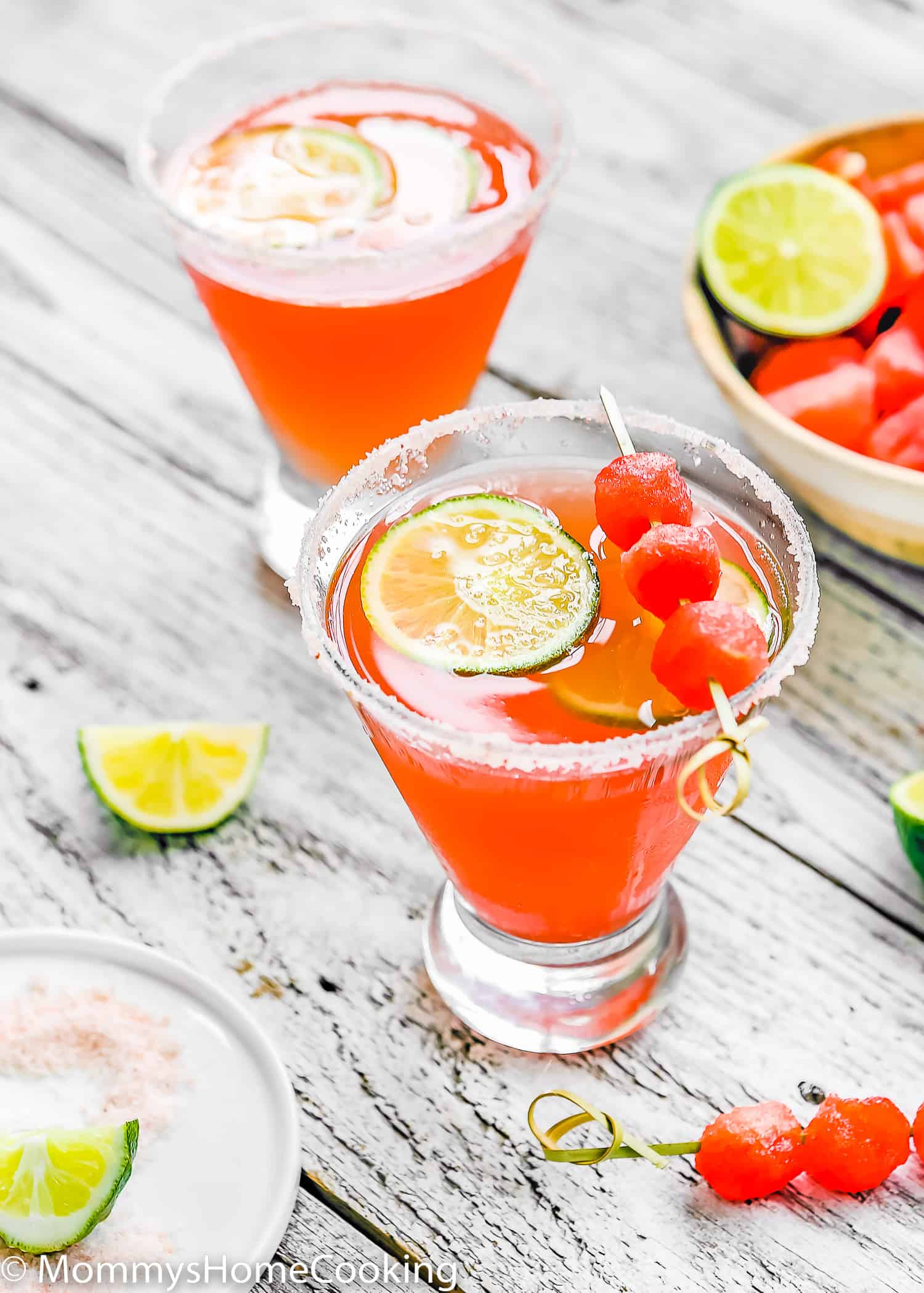 two Watermelon Cocktails over a wooden surface surrounded by lemon slices.